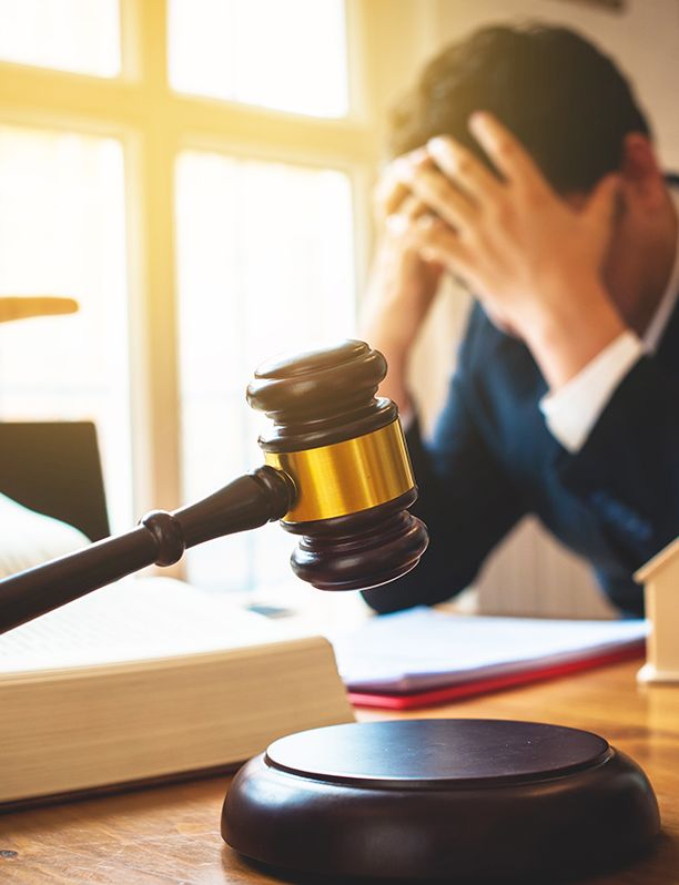 a man is sitting at a table with his head in his hands while a judge holds a gavel in front of him .