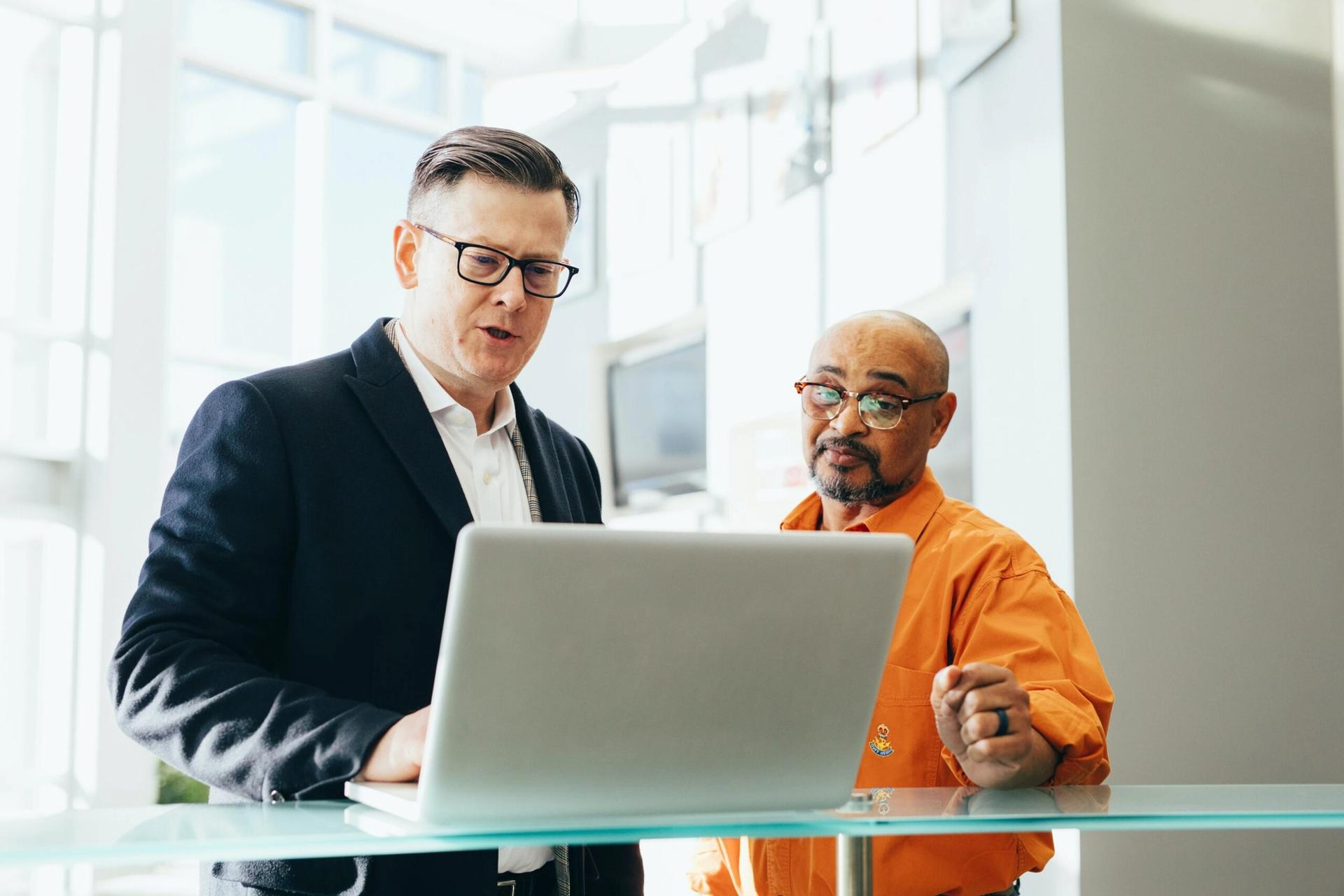 two men are standing next to each other looking at a laptop computer .