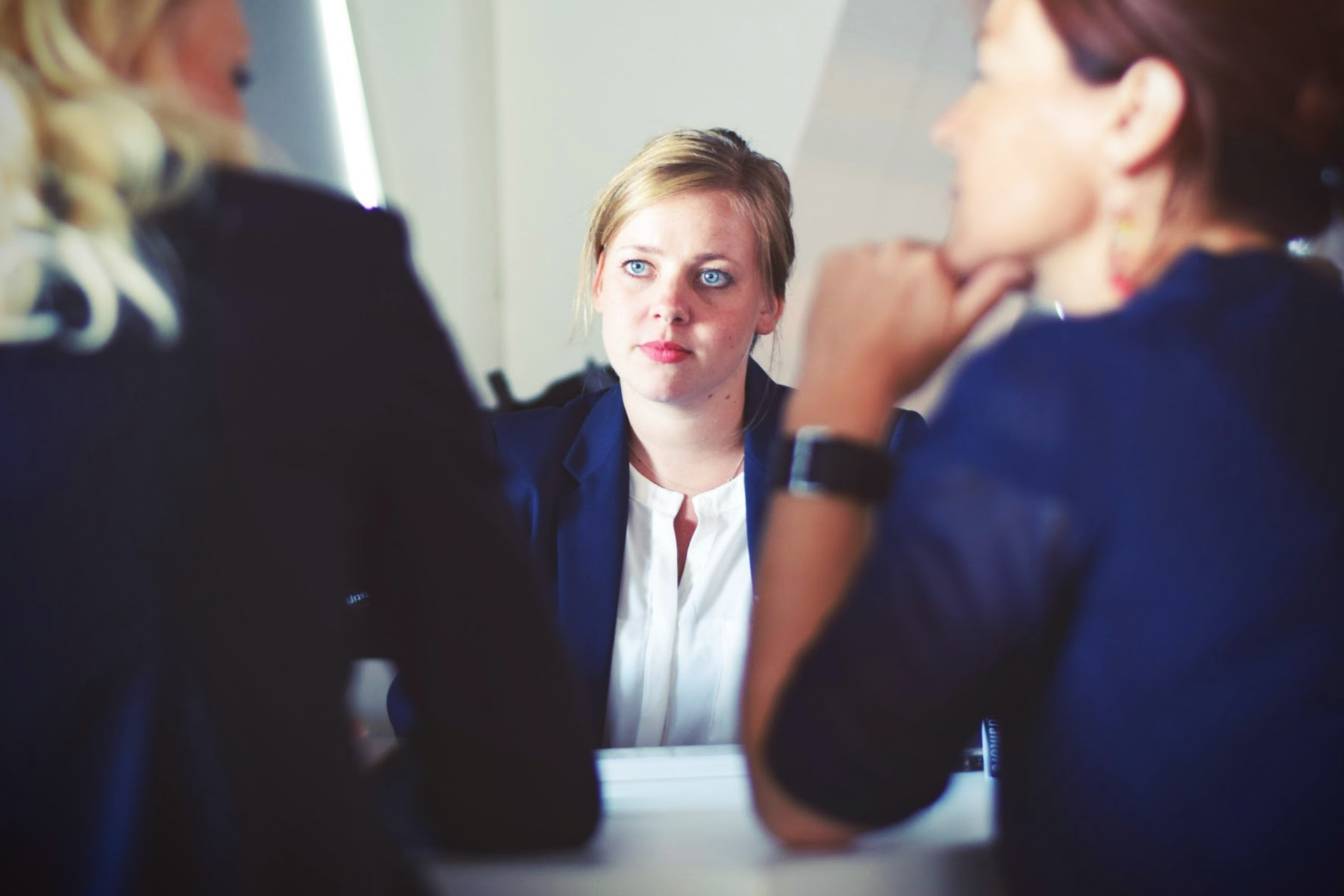 A woman in a blue blazer intently listens during a meeting with two other women.