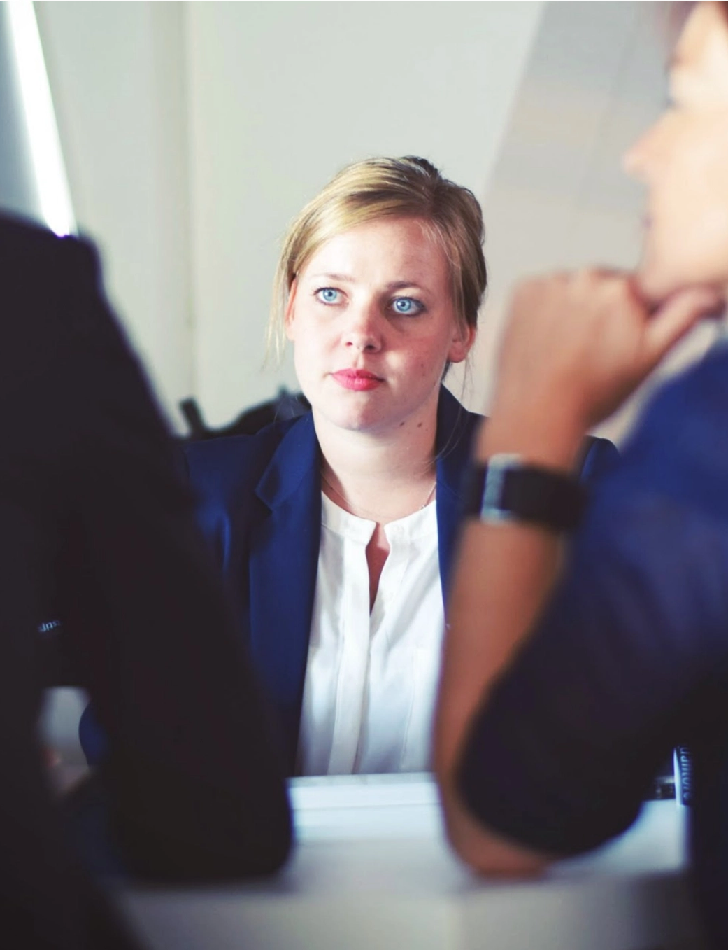 A woman in a blue blazer intently listens during a meeting with two other women.
