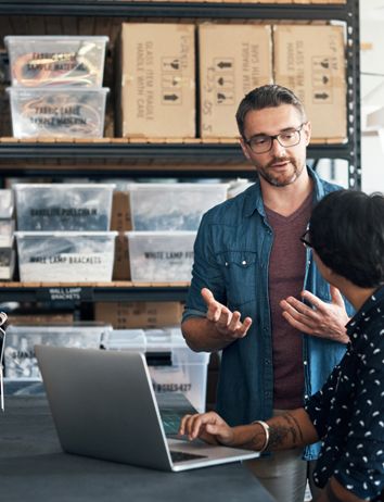 a man and a woman are talking in a warehouse while looking at a laptop .