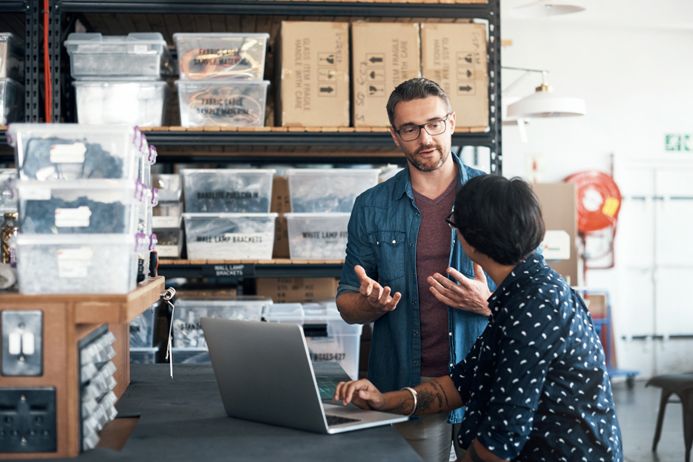 a man and a woman are talking in a warehouse while looking at a laptop .