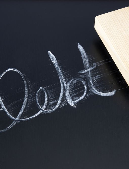 the word debt is being erased on a blackboard with a wooden eraser .