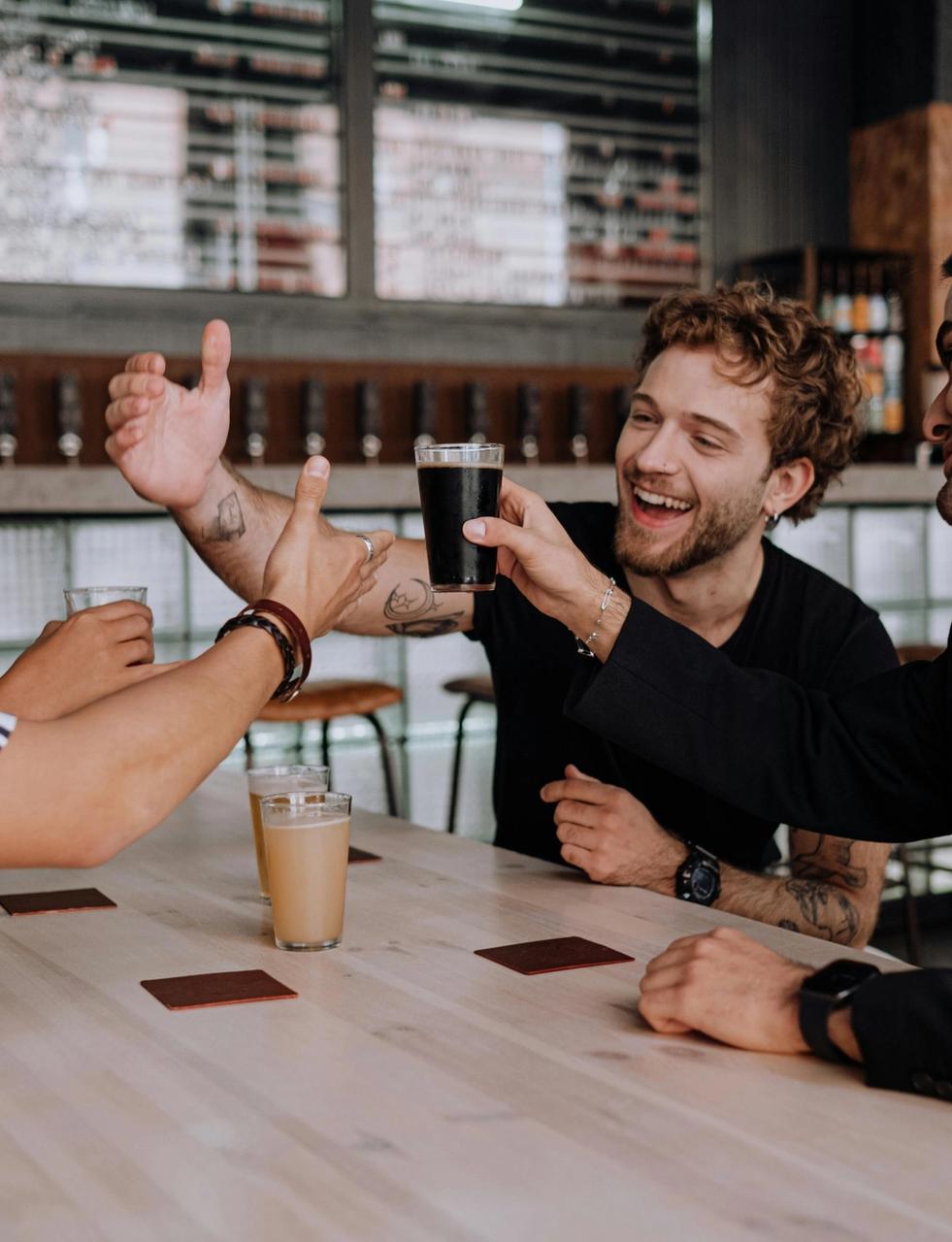 Four friends smiling and making a toast with drinks at a bar.