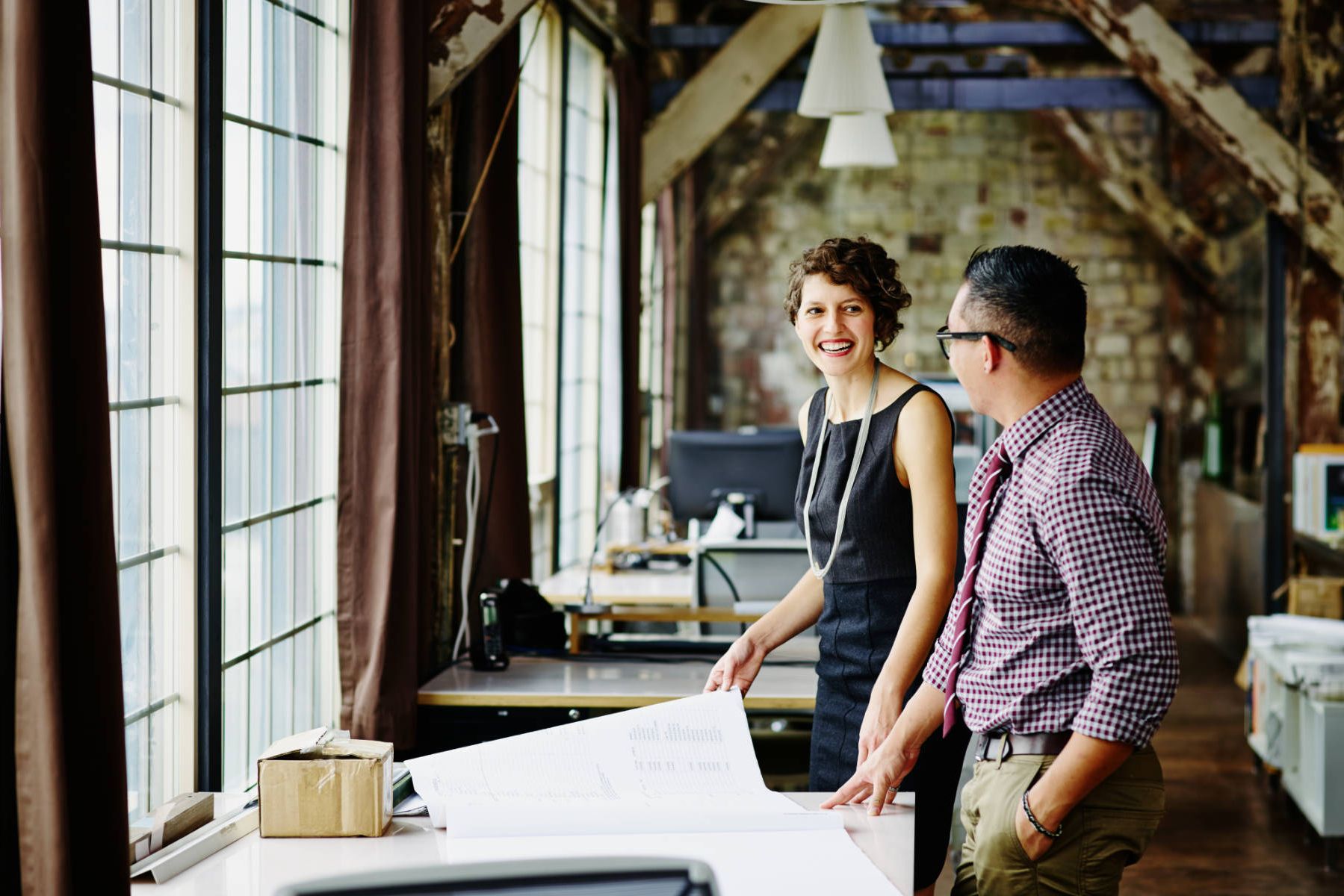 a man and a woman are standing in an office looking at a blueprint .