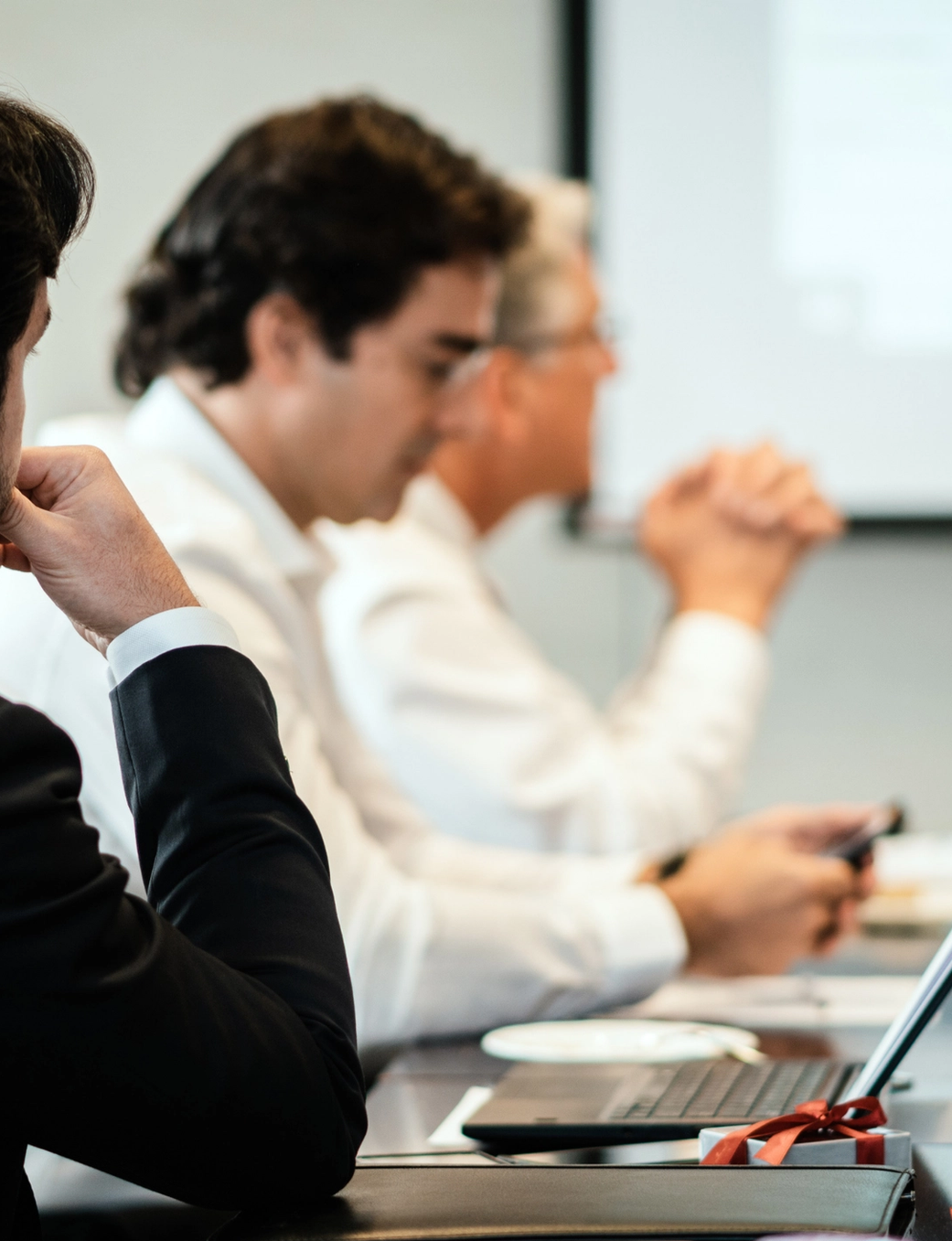Man in a black suit contemplating during a business meeting with other attendees.