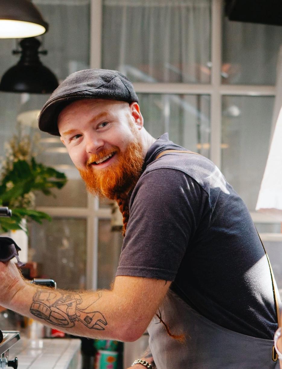 a man with a beard is cleaning a coffee machine in a cafe .