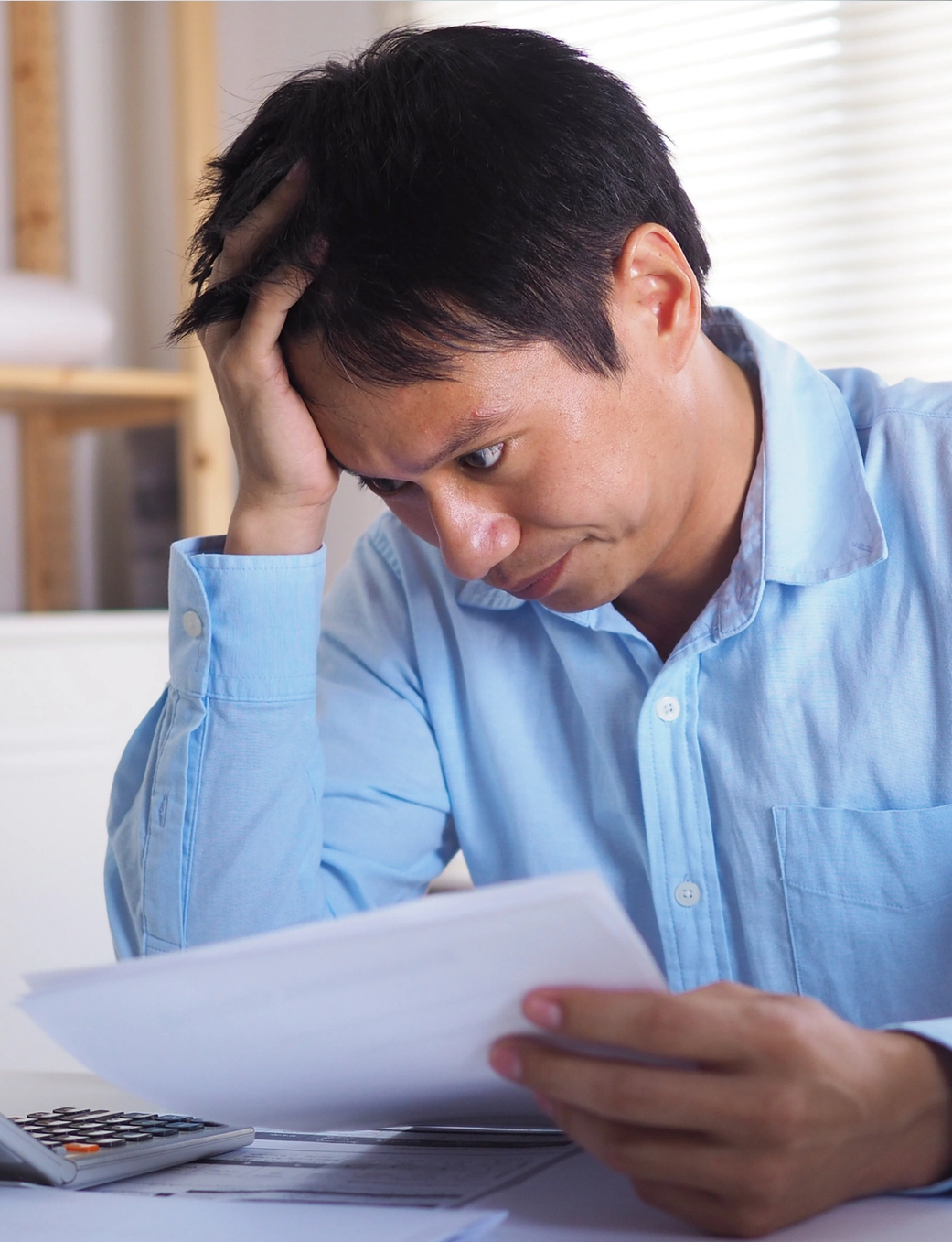 Stressed man with hand on head reviewing documents.