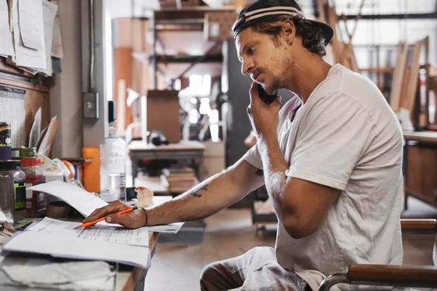 a man is sitting at a desk talking on a cell phone .