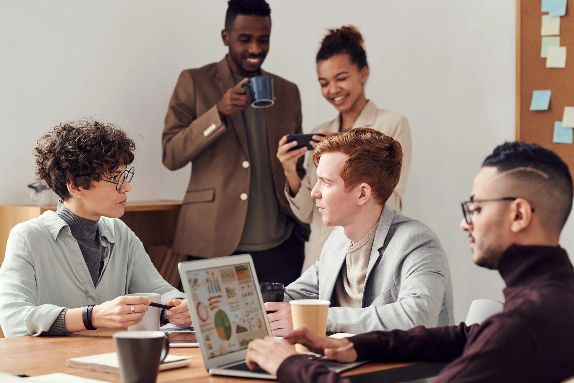 a group of people are sitting around a table with laptops and cups of coffee .
