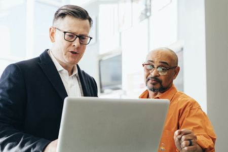 two men are looking at a laptop computer together .
