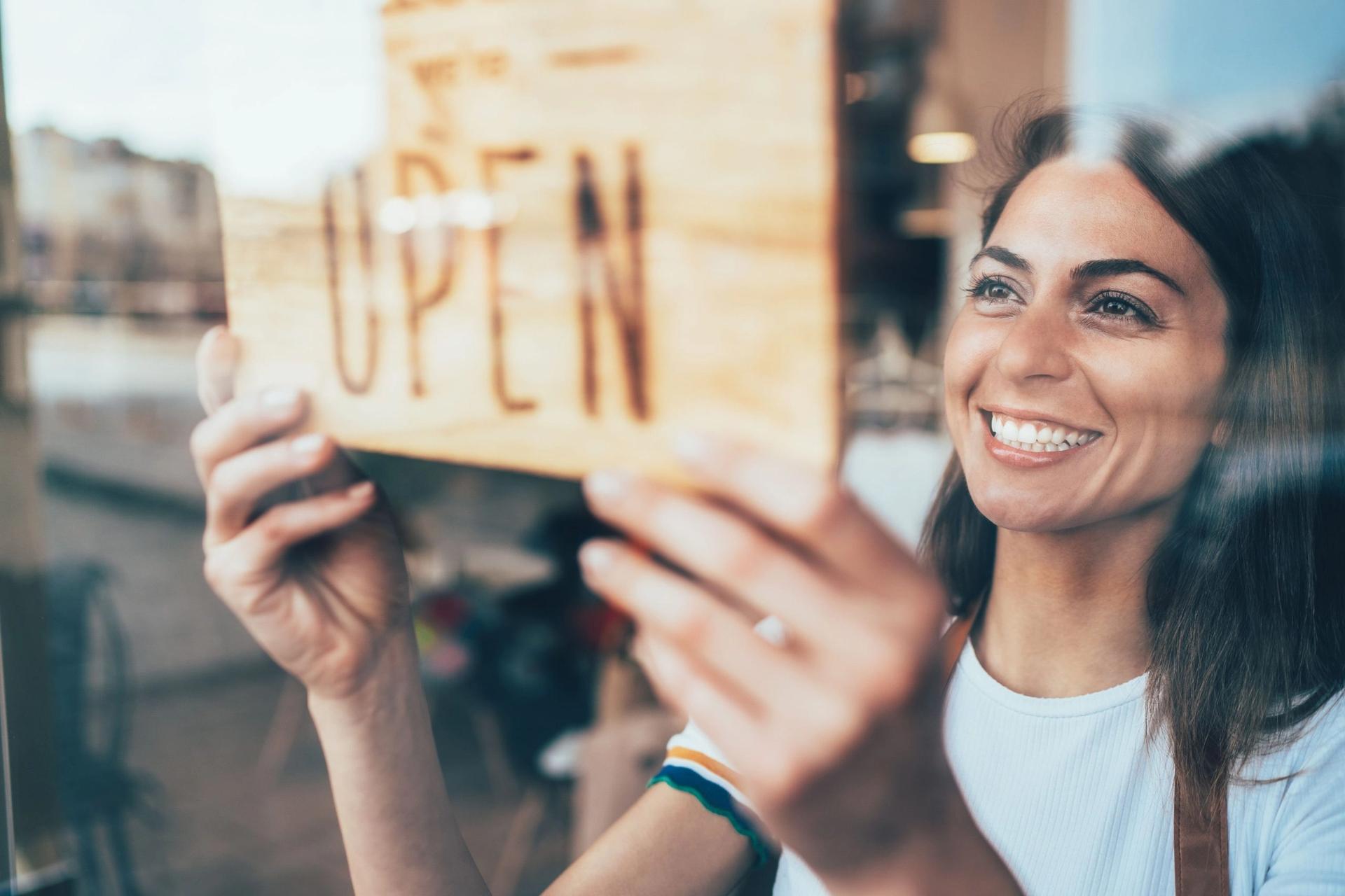 a woman is holding an open sign in front of a store window .