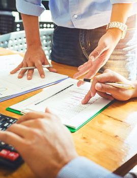 Two people reviewing financial documents and using a calculator on a wooden desk.