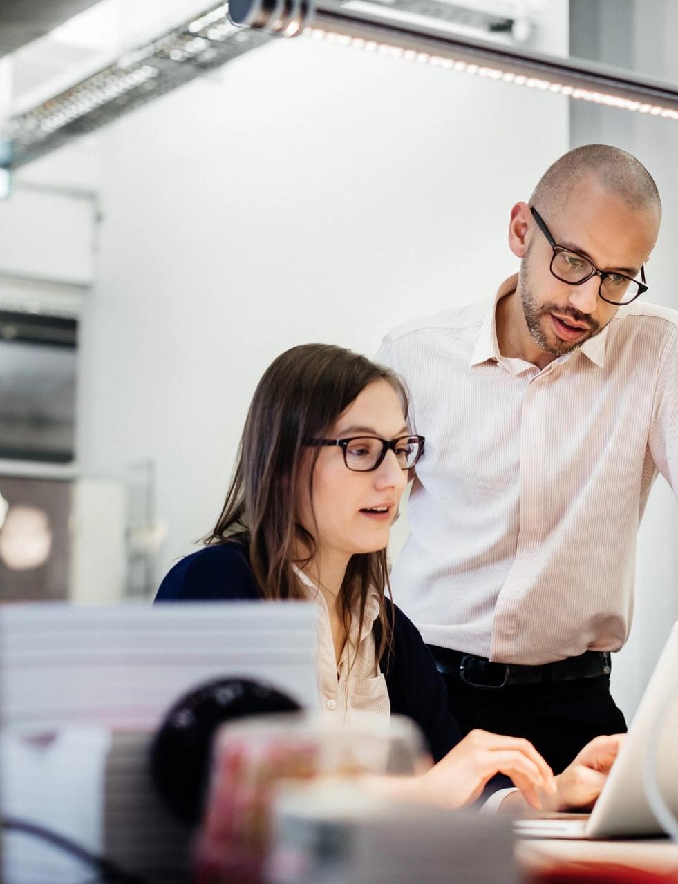 a man and a woman are looking at a laptop computer in an office .
