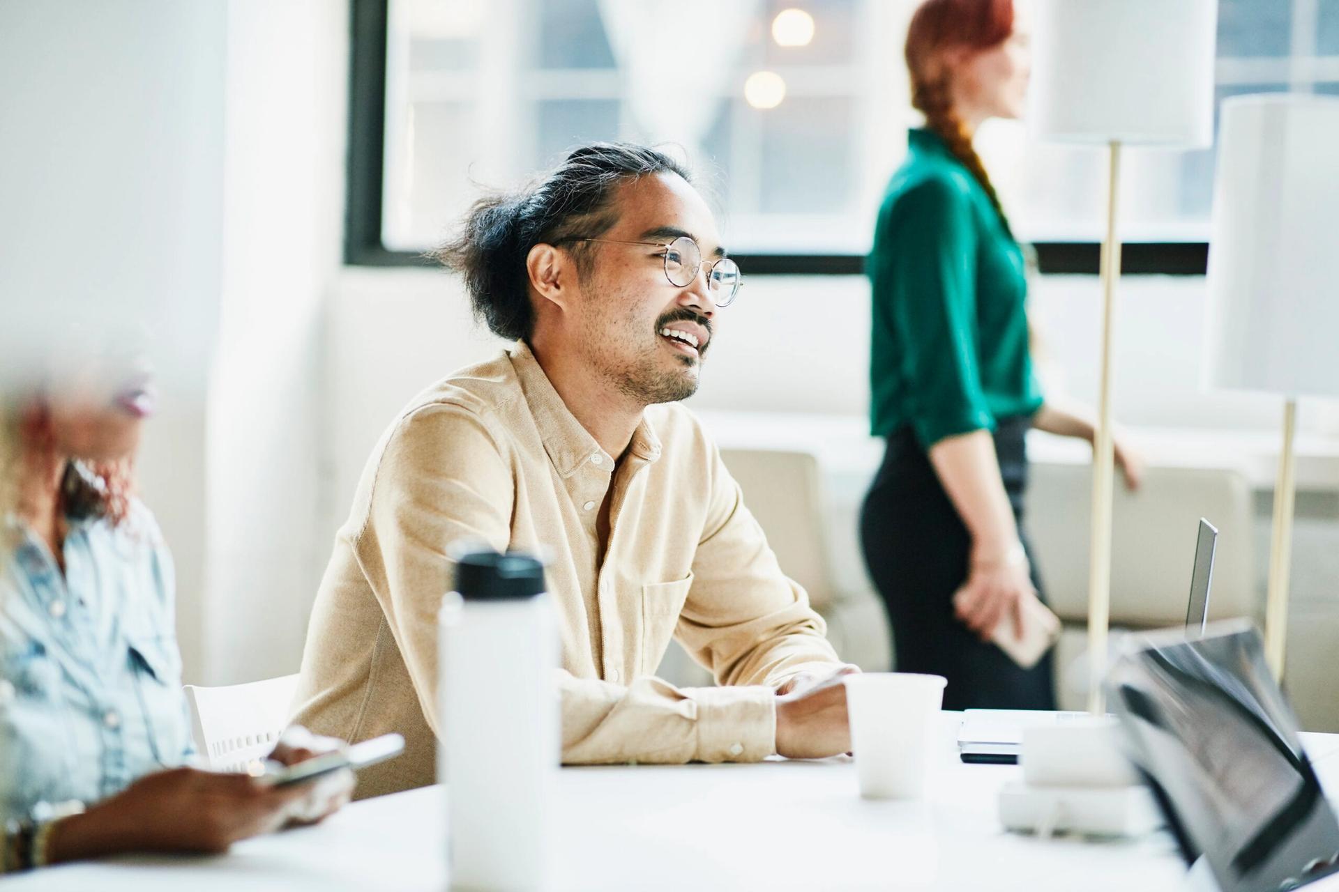 a man is sitting at a table with other people in an office .