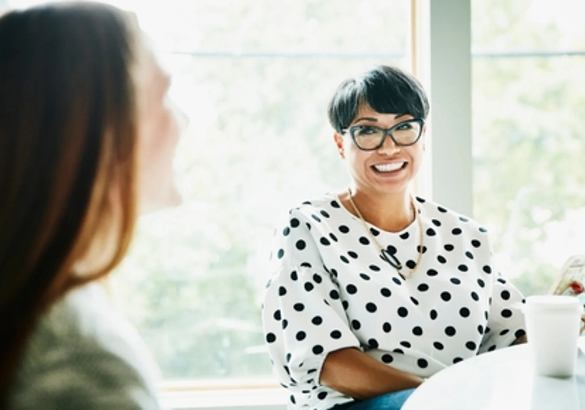 a woman in a polka dot shirt is sitting at a table talking to another woman .