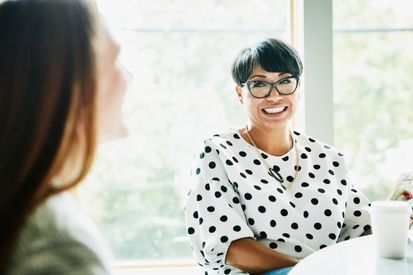 a woman in a polka dot shirt is sitting at a table talking to another woman .