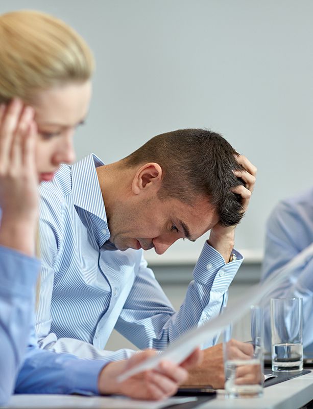 a group of business people are sitting at a table with their hands on their heads .