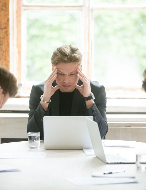 a group of businessmen are sitting around a table with their hands on their heads .