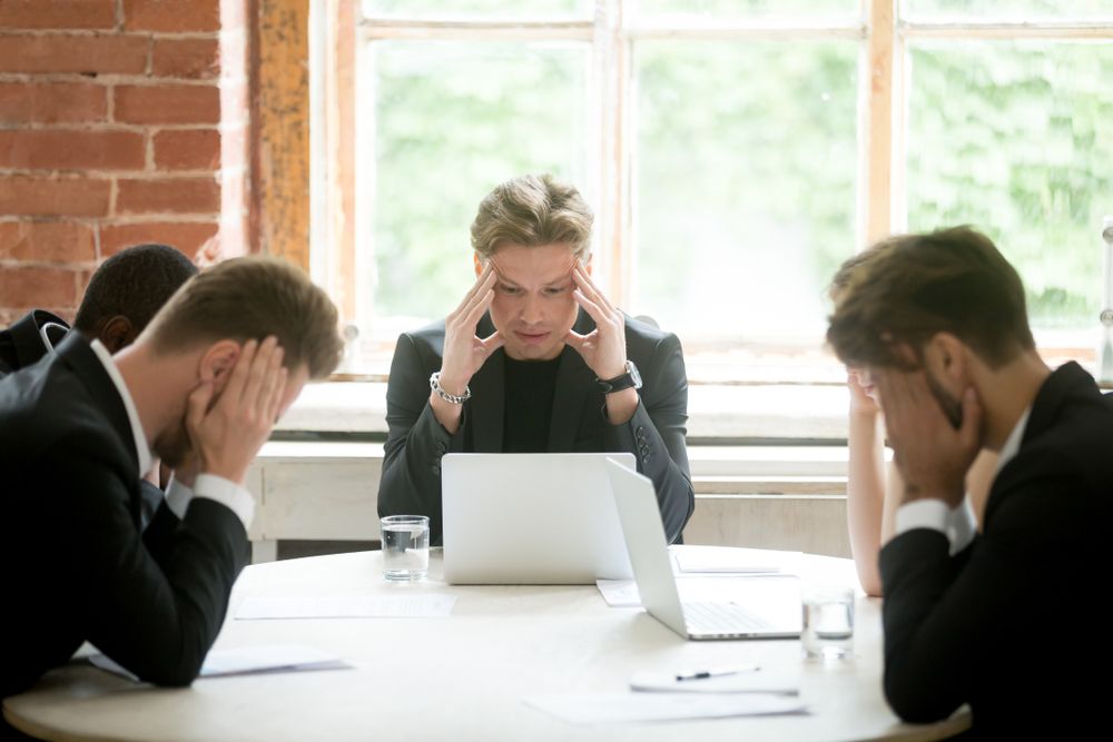 a group of businessmen are sitting around a table with their hands on their heads .