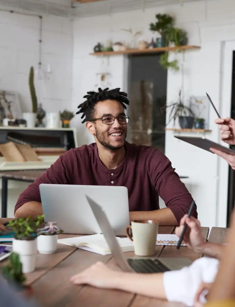 a group of people are sitting around a table with laptops .