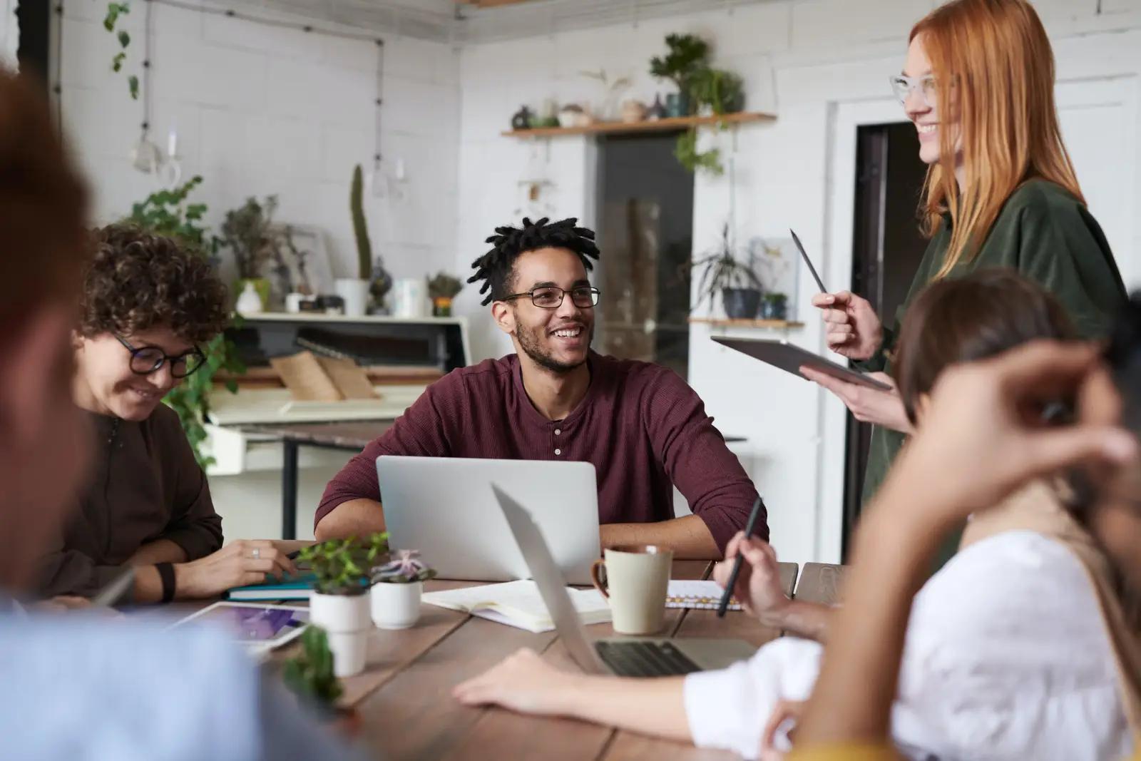 a group of people are sitting around a table with laptops .