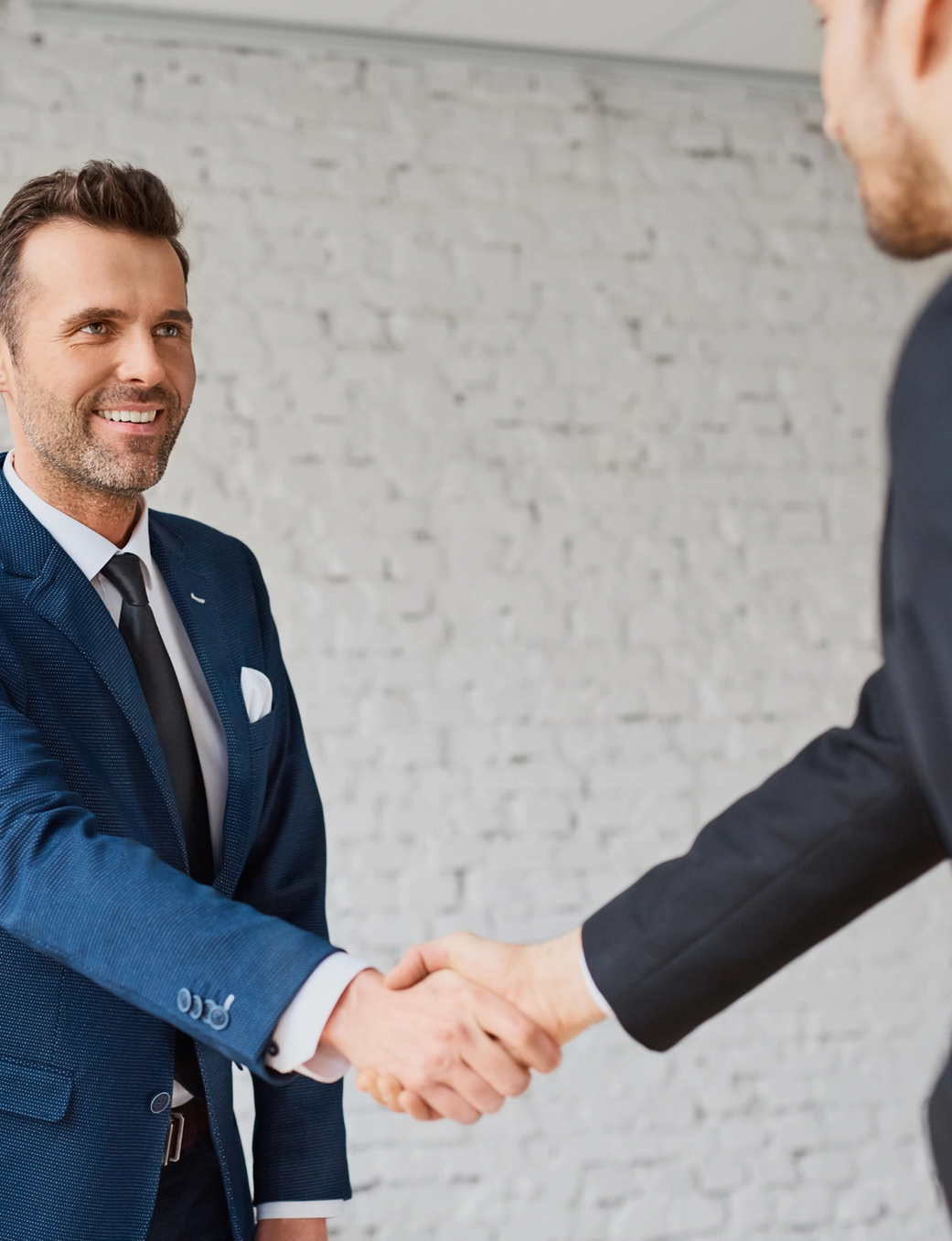 Two businessmen in suits shake hands.