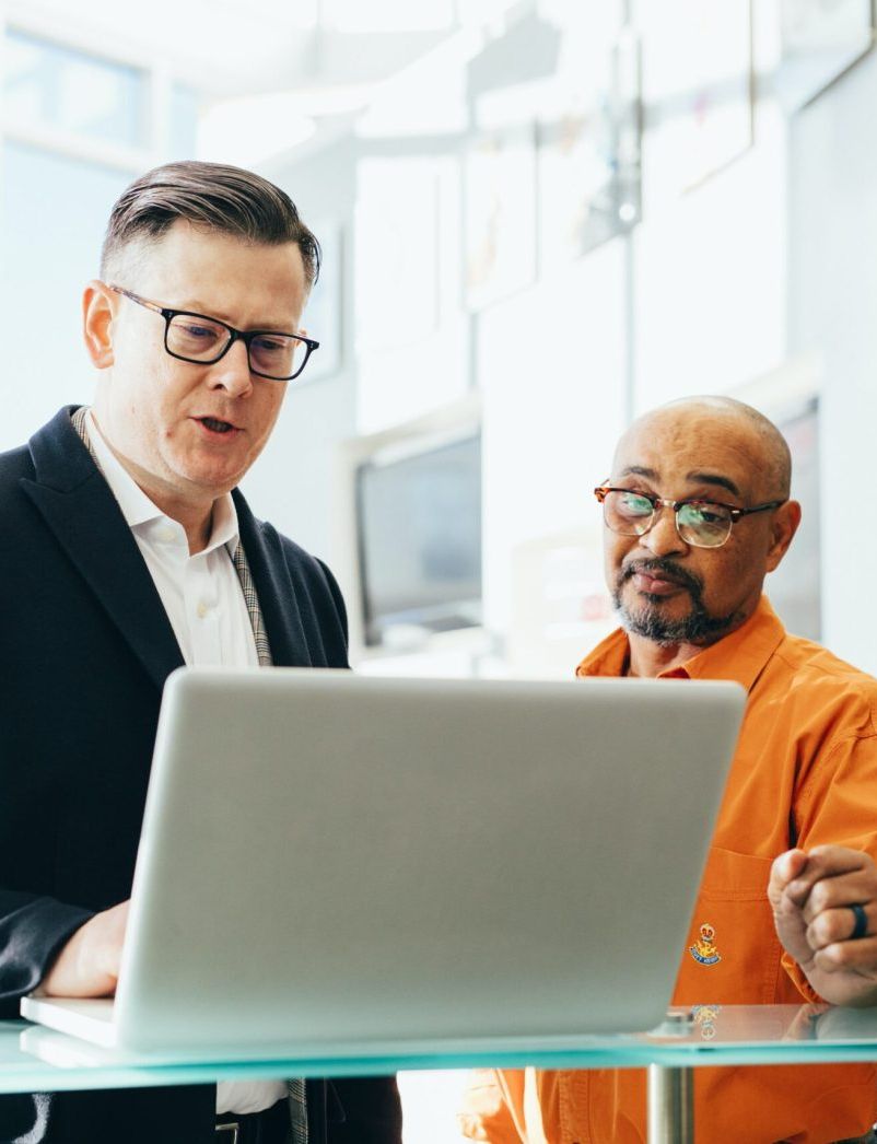 Two men looking at a laptop and discussing something in an office setting.