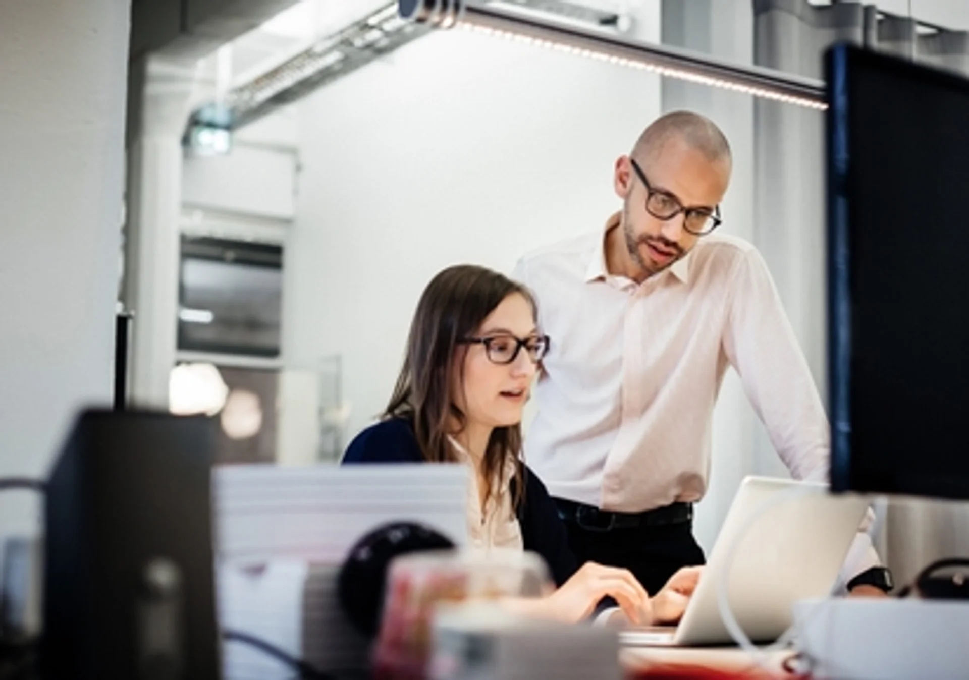 a man and a woman are looking at a laptop computer in an office .