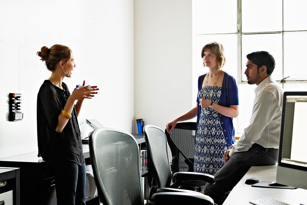 three people are standing in an office talking to each other
