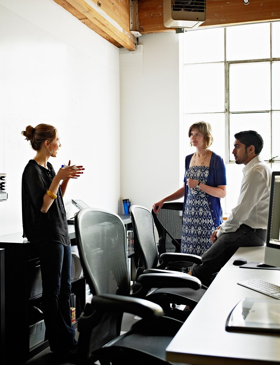 three people are standing in an office talking to each other