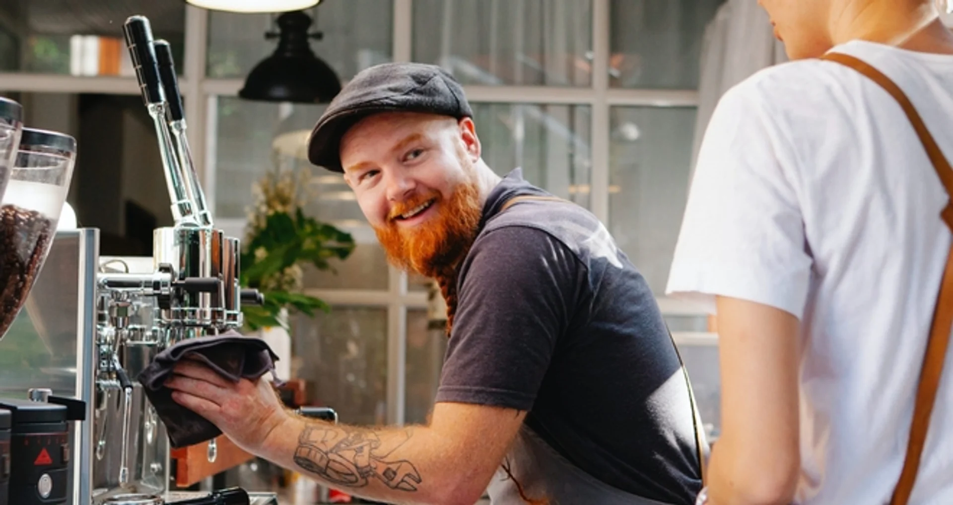 a man with a beard is cleaning a coffee machine in a cafe .