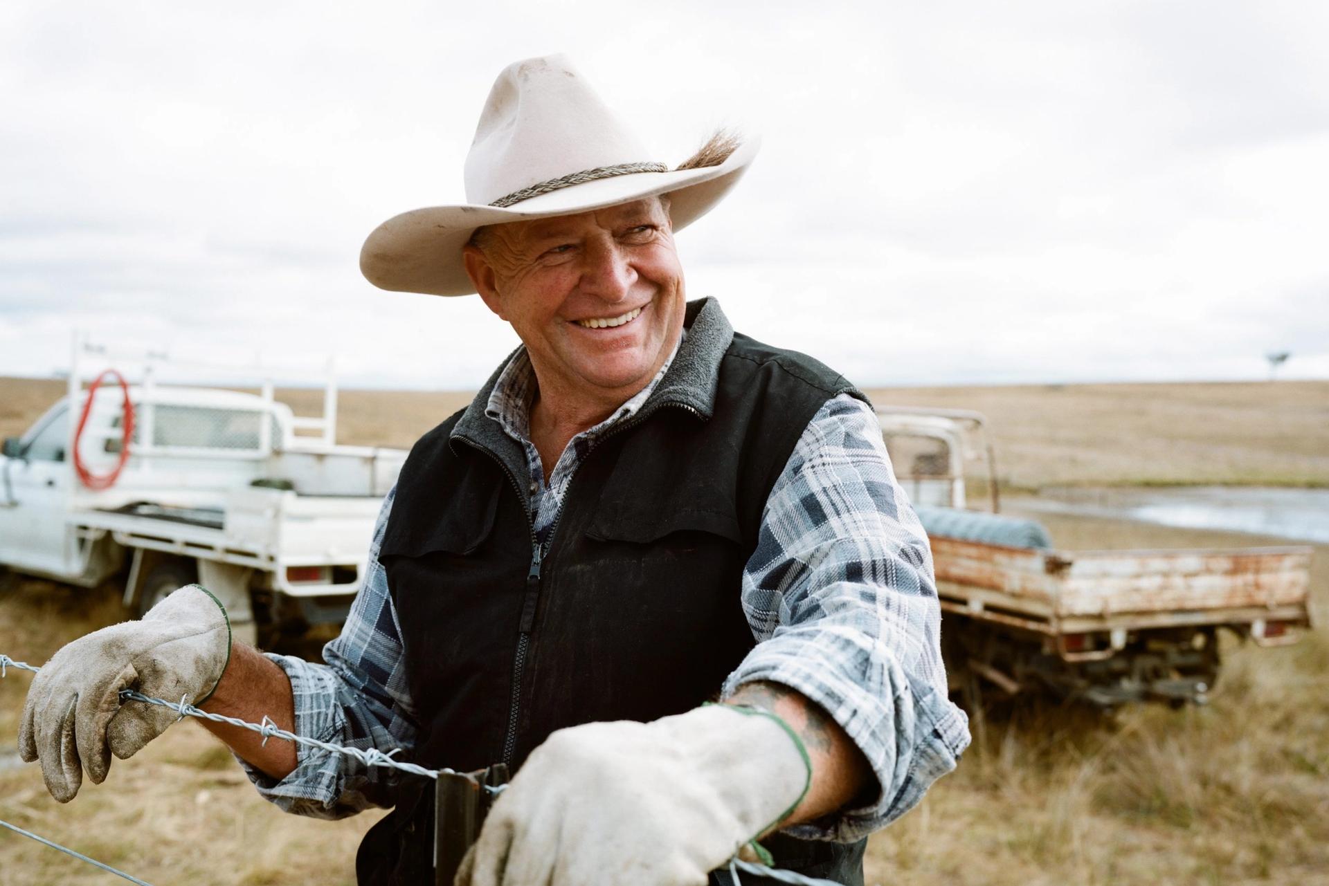a man in a cowboy hat is working on a barbed wire fence .