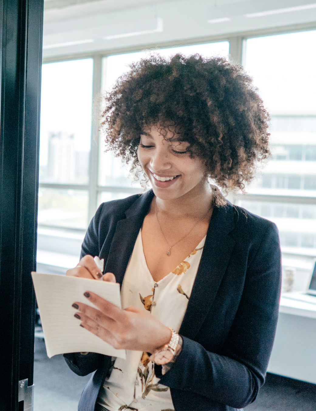 Smiling woman with curly hair writing notes in an office.
