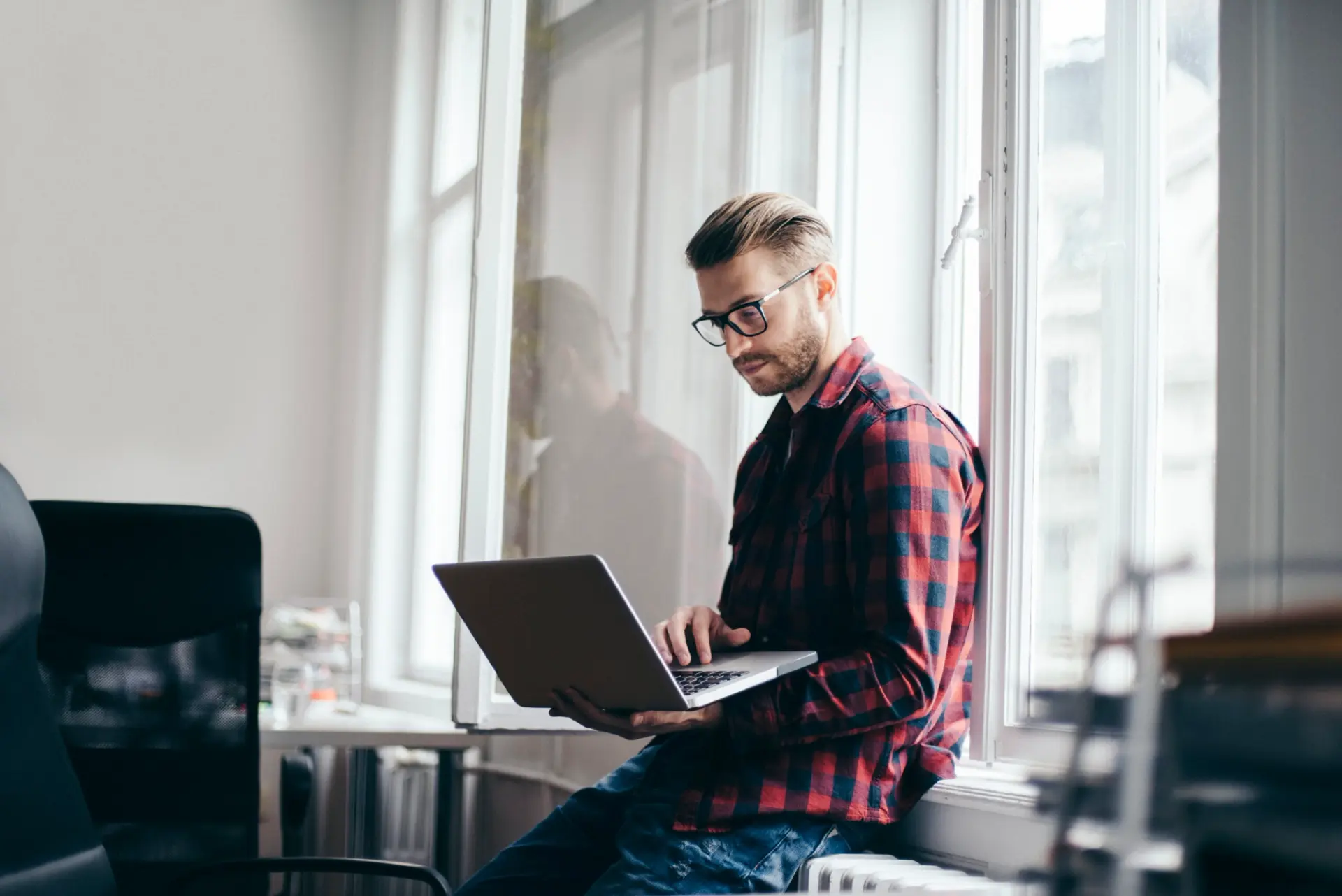 a man is sitting on a window sill using a laptop computer .