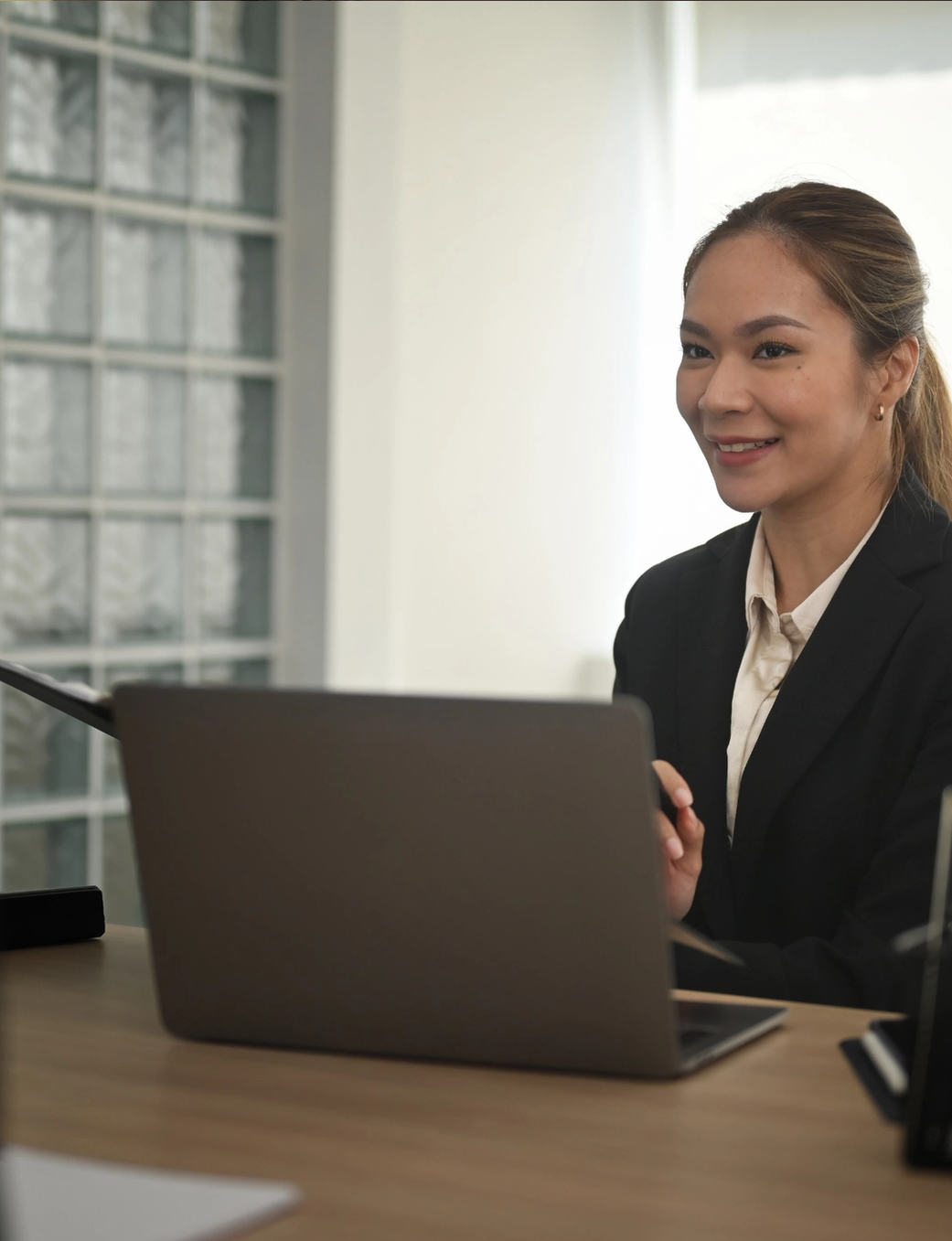 Smiling businesswoman in a suit at a desk with a laptop, in a meeting.