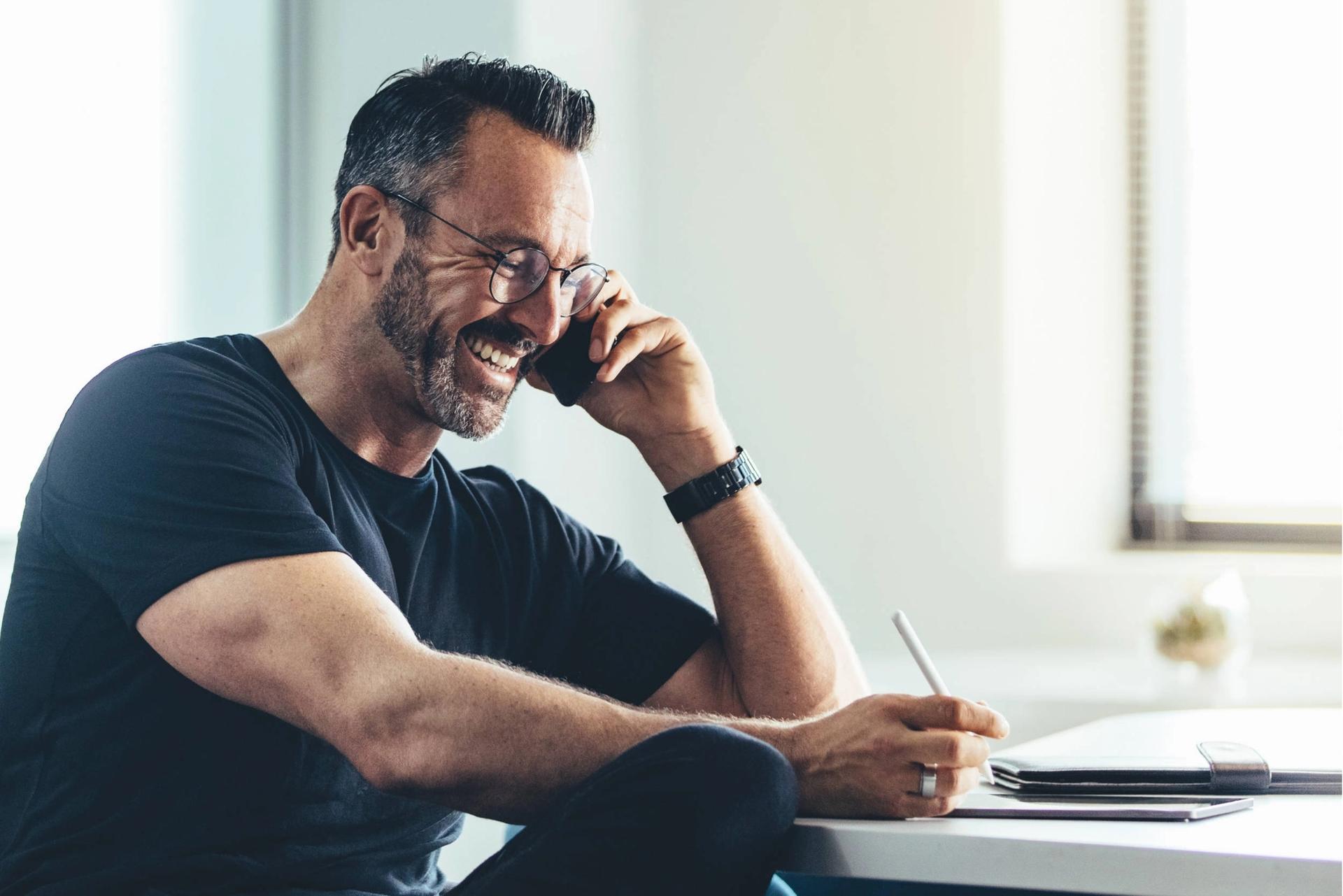 a man is sitting at a desk talking on a cell phone .