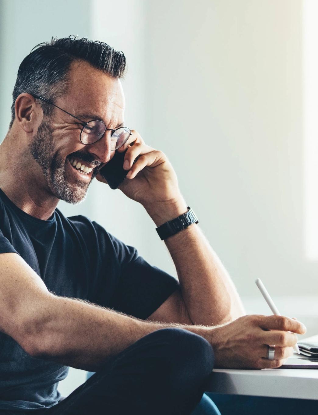 a man is sitting at a desk talking on a cell phone .