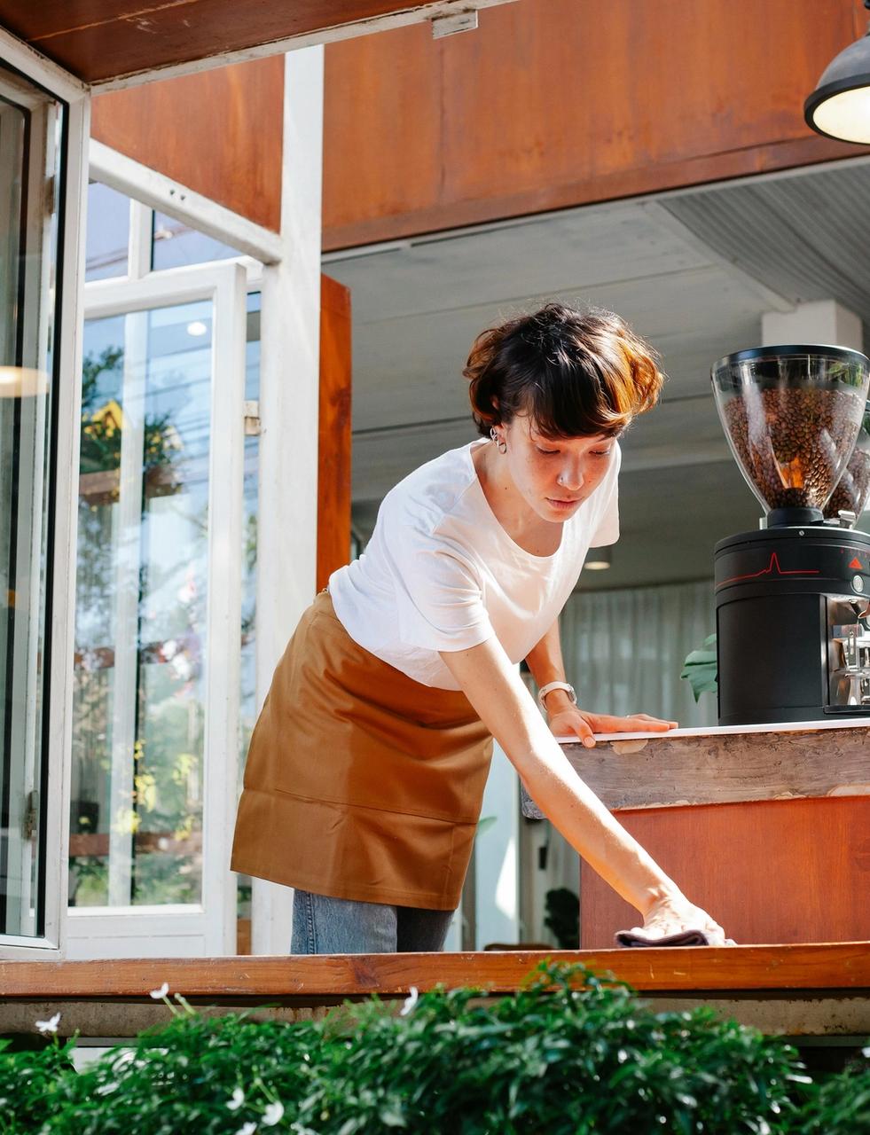 A woman in an apron cleans a cafe counter.