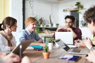 a group of people are sitting around a table with laptops .