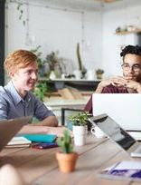 a group of people are sitting around a table with laptops .