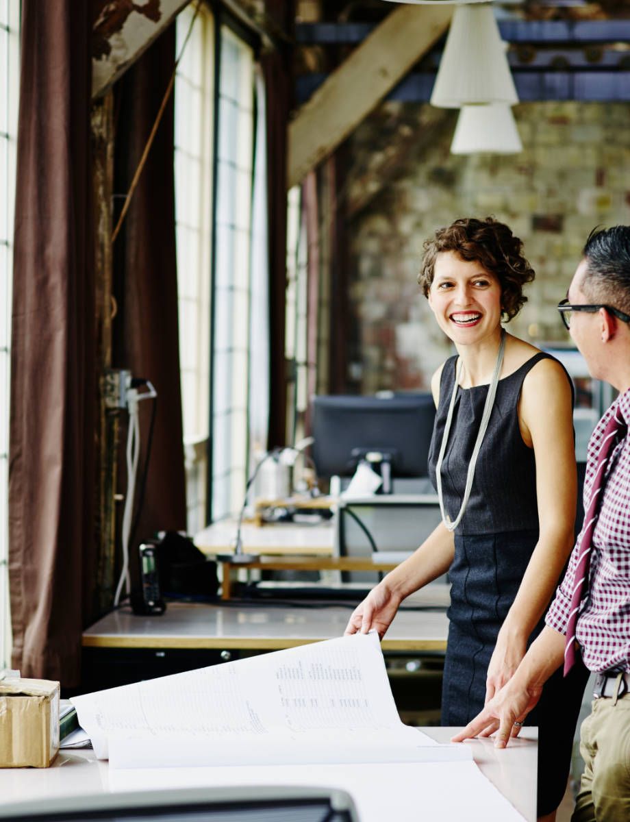 a man and a woman are standing in an office looking at a blueprint .