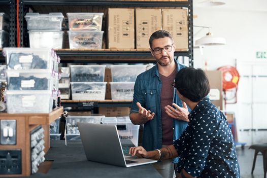 a man and a woman are talking in a warehouse while looking at a laptop computer .