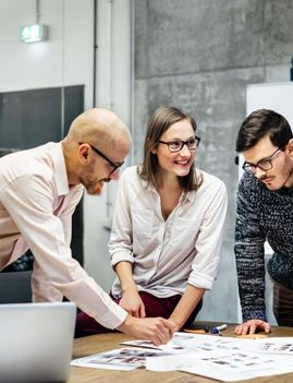 a group of people are standing around a table looking at a laptop .