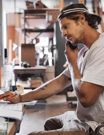 a man is sitting at a desk talking on a cell phone .