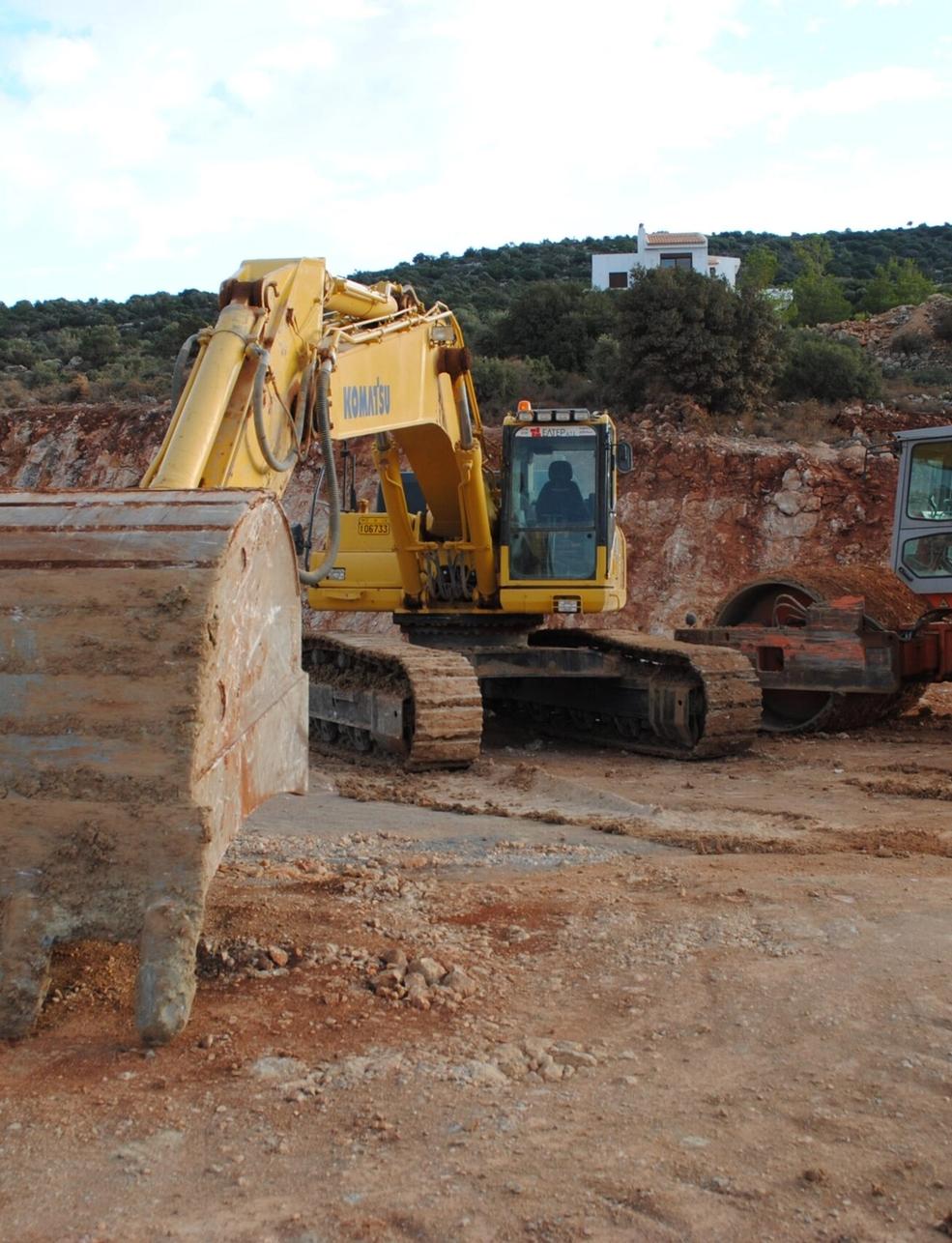 a yellow excavator and a red dump truck are parked in a dirt field .