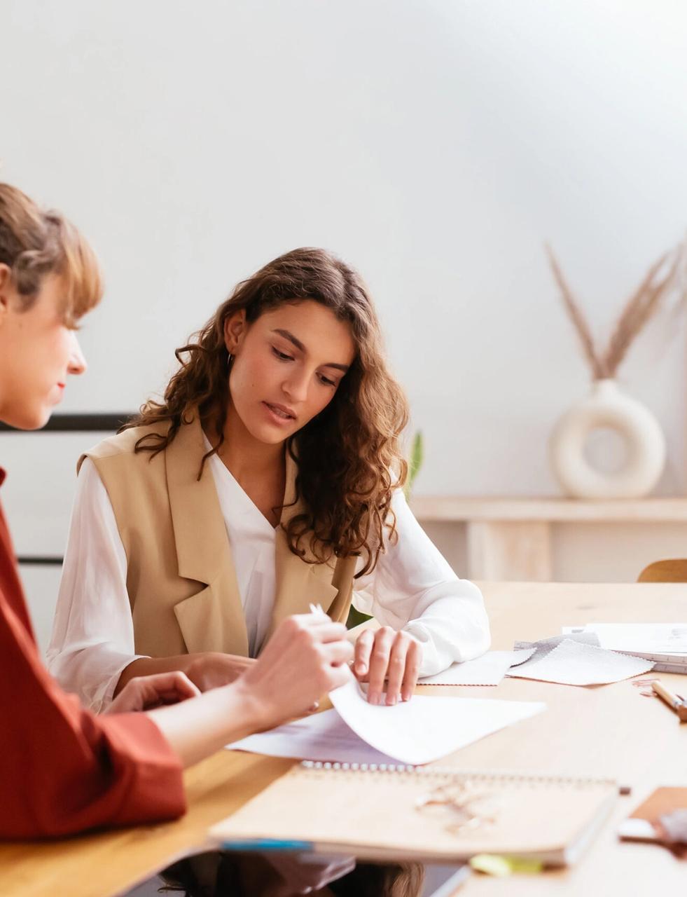 two women are sitting at a table looking at papers .