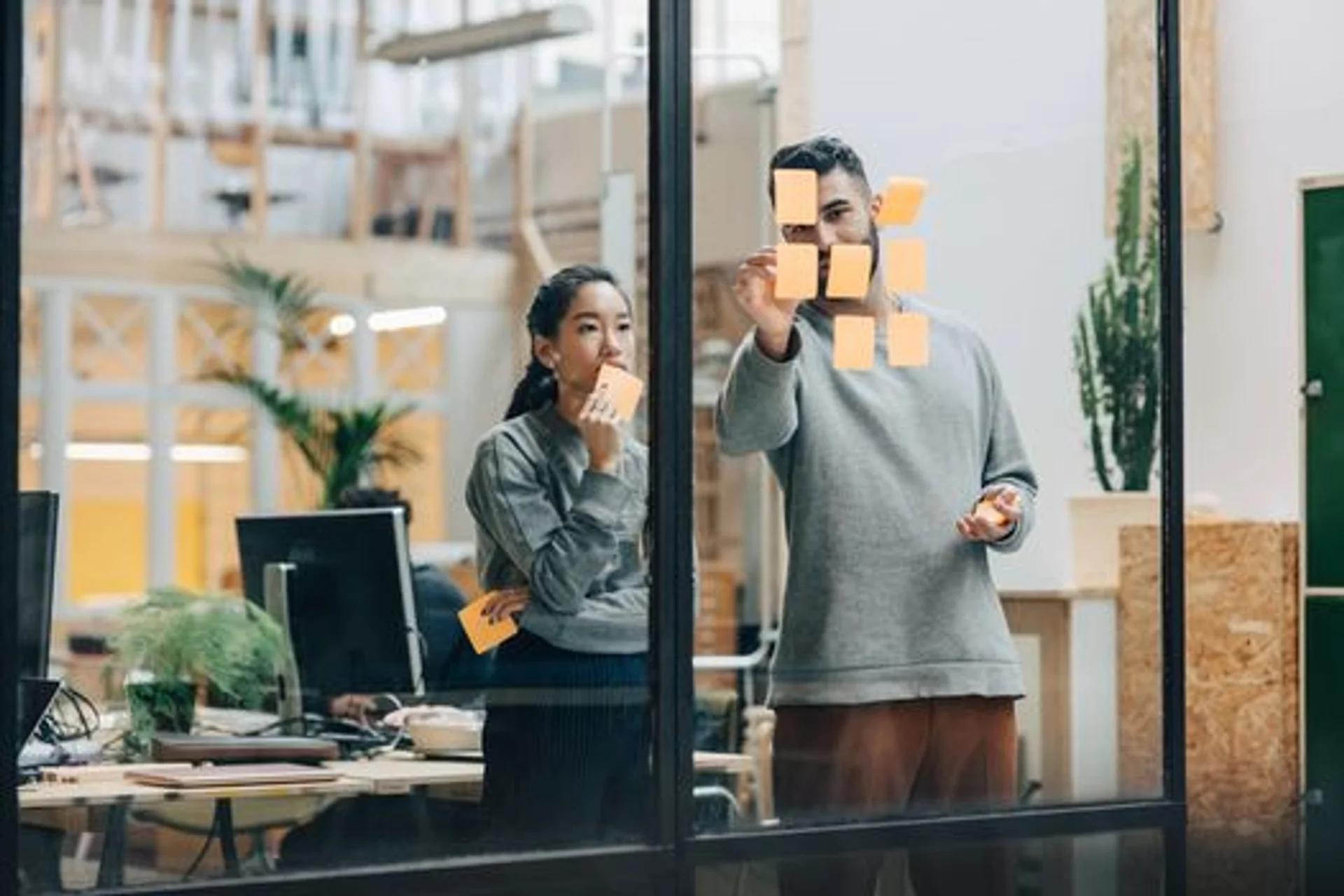 a man and a woman are looking at sticky notes on a glass wall .