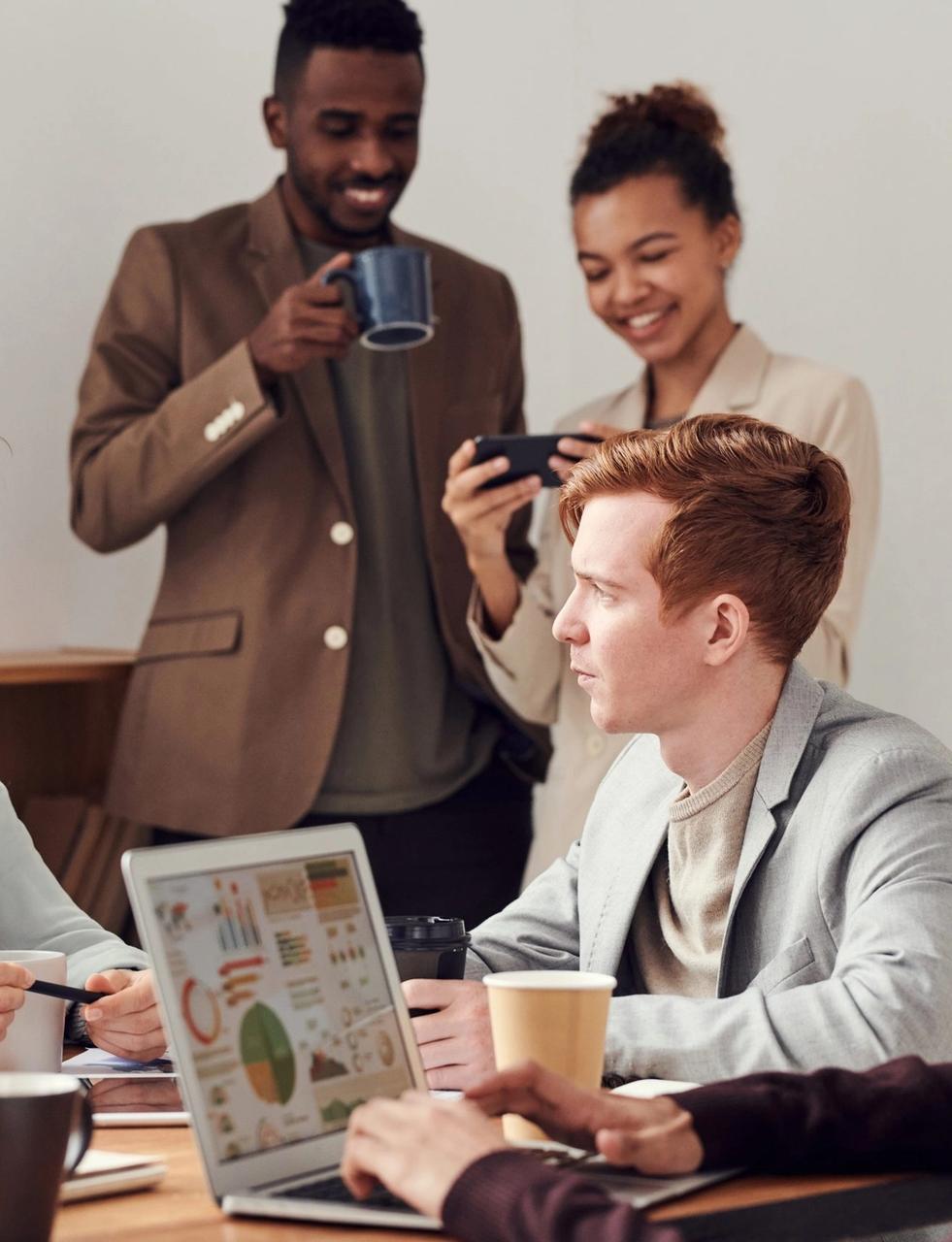 a group of people are sitting around a table with laptops and cups of coffee .