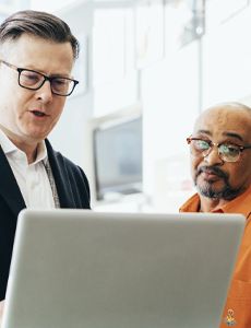 two men are looking at a laptop computer together .